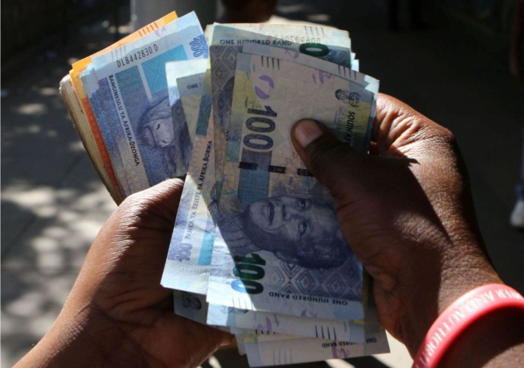 A stack of R100 and R200 notes being counted by two hands