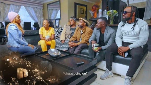 Six black family members sitting on the couch in the living room focused on one of the ladies sharing news with them